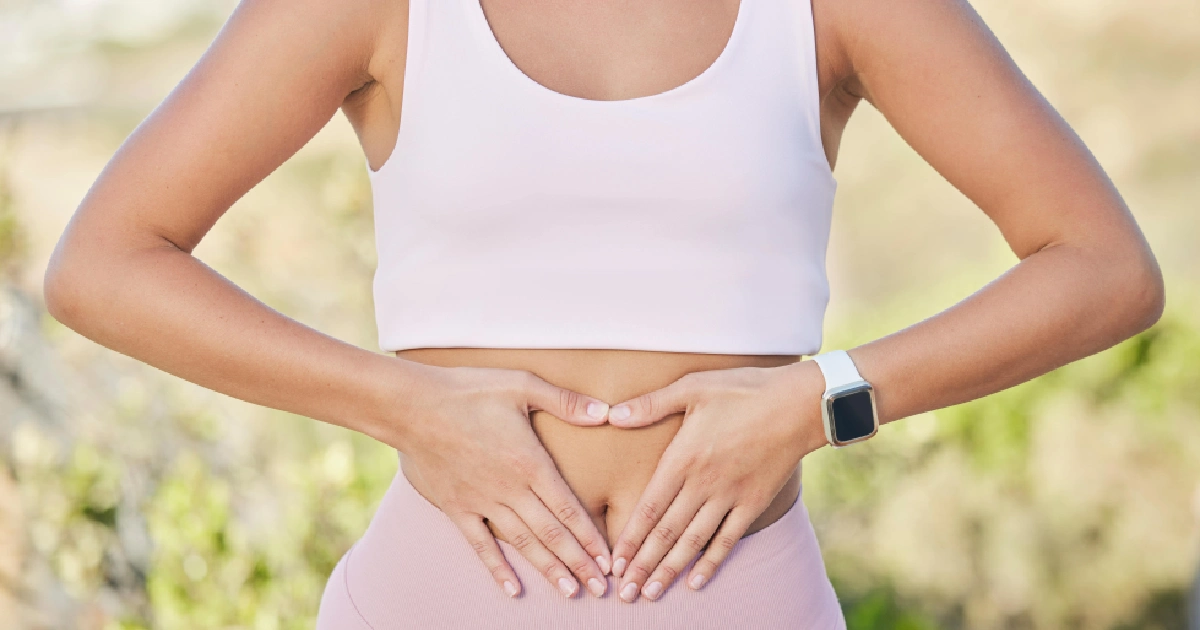 A woman in pink activewear makes a heart over her abdomen outdoors during a Gut Health Optimization session in Lacey, WA.